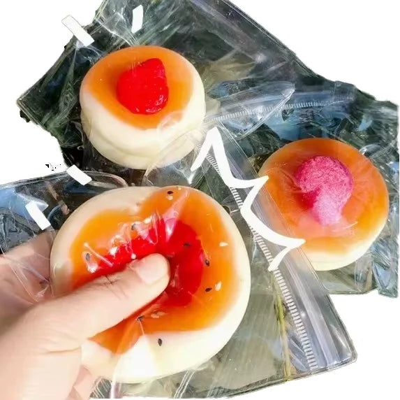 Three packaged buns with red and pink toppings, held in a hand, clear wrapping visible.